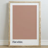 A framed print featuring a solid flat white color swatch above the text "Flat white." in a minimalist style, set against a light wall and wooden floor.