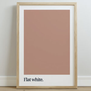 A framed print featuring a solid flat white color swatch above the text "Flat white." in a minimalist style, set against a light wall and wooden floor.