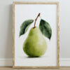A framed watercolour art print of a green pear with two leaves, set against a white background, displayed on a light wooden floor.